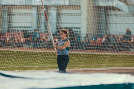 Pole vaulting indoors - young woman with pigtails standing near the mat holding a poleの写真素材