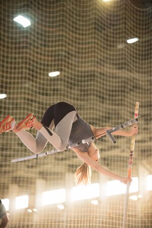 Pole vaulting in the sports stadium - young sportive woman with ponytail jumping over the barの写真素材