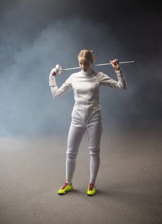 A young woman fencer standing in the studio with a sword behind her shoulders