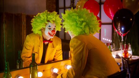 A crazy man clown in full costume looking in the mirror and smilingの写真素材