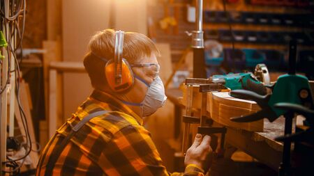 Carpentry indoors - a man woodworker setting a polishing machine on the detail to polish the sidesの写真素材