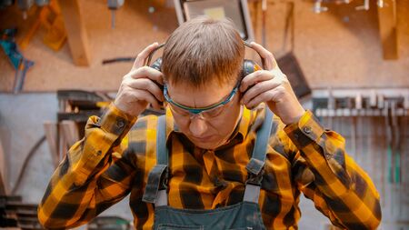 Carpentry indoors - a man woodworker put on a protective soundproof headphonesの写真素材