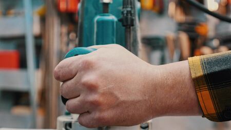 Carpentry indoors - a woodworker polishes the wooden detail from the top in the workshop - holding the polishing machineの写真素材