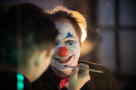 Clown concept - Make-up artist applying paint on the man clown in the dressing roomの写真素材