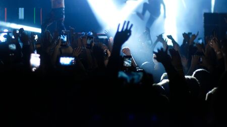 Energetic crowd dancing with their hands up at the punk concert - blue lighting. Mid shotの写真素材