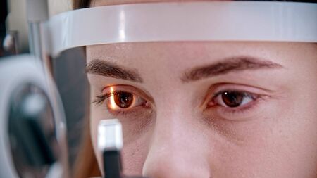 A young woman with pink lips checking her visual acuity with a light of special big optometry machineの写真素材