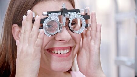 Ophthalmology treatment - a young smiling woman putting on a device for vision test. Mid shot