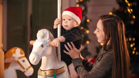 Christmas decorated studio - A smiling young mother standing near by her baby on carousel