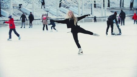 A young blonde woman professional figure skater skating on the outdoors ice rink around peopleの写真素材