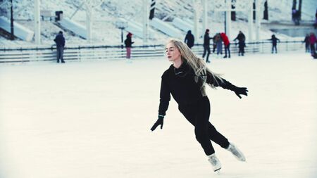 A young blonde attractive woman professional figure skater skating on the ice rink around peopleの写真素材