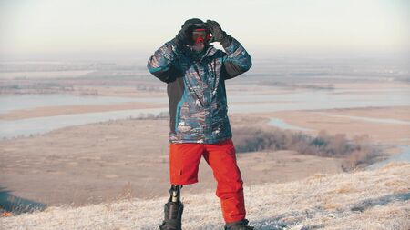 Snowboarding - A man with prosthetic leg standing on the board and putting on protective glasses....