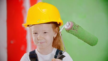 Happy little girl in a helmet is holding a paint roller and looking at the cameraの写真素材
