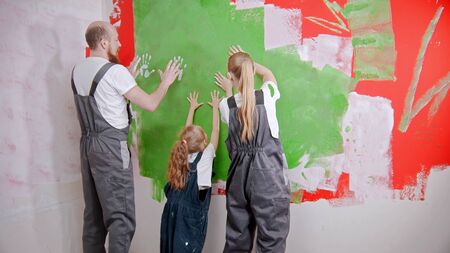Happy family are putting their white handprints on a green wall
