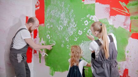 Happy family are putting their white handprints on a green wall - dad drawing something on the wall....