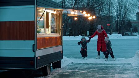 A young woman mother with her children walking out from the ice rink to a little shop. Mid shot
