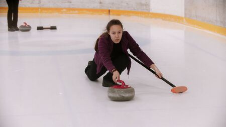 Curling - a woman pushes off in the ice field with a granite stone