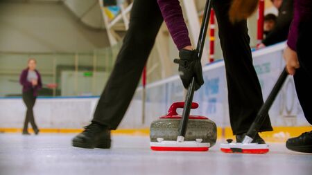 Curling training - leading granite stone on the ice - clearing the ice before the stone. Mid shotの写真素材
