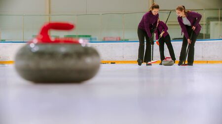 Curling training - leading granite stone on the ice - two women rubbing the ice before the stone. Mid shotの写真素材