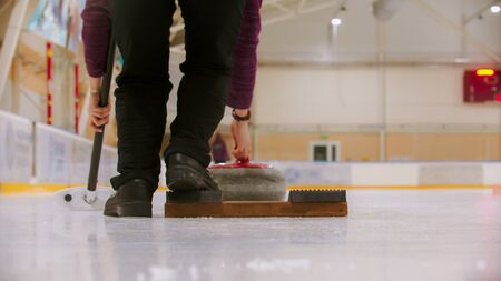 Curling training indoors - a woman about to push off the stand on the ice field. Mid shot