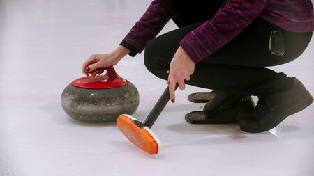 Curling training - woman holding a granite stone with red handle and holding a special brush. Mid...