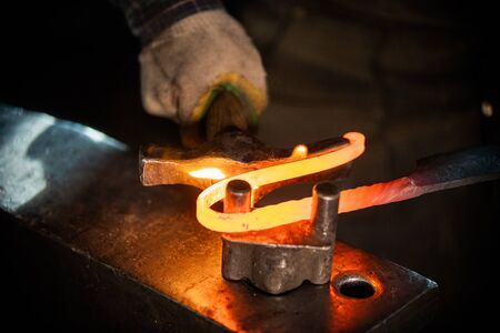 A man blacksmith making a unique handle for the knife - bending the metal. Mid shotの写真素材