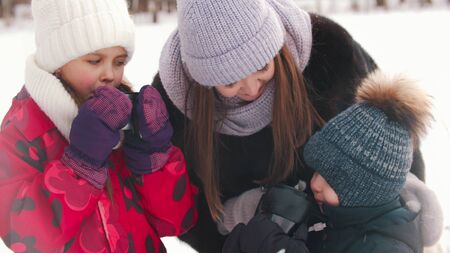Mother with two little kids standing outdoors drinking hot drinksの写真素材
