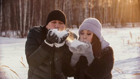 A married cute couple blowing out snow from their handsの写真素材