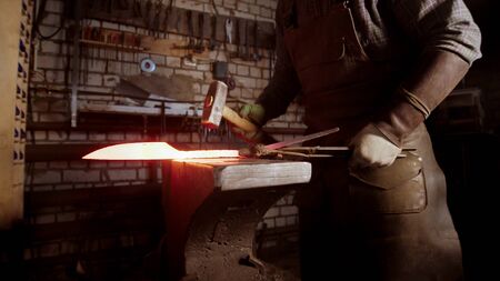 A man blacksmith forging a hot knife blade using a hammerの写真素材