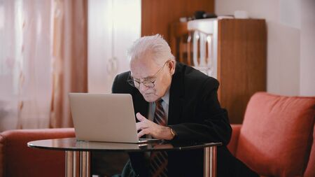 An old man in glasses typing something in a laptopの写真素材