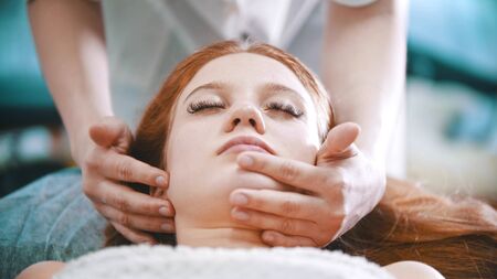 Massage - masseuse kneading the chin area to a young woman using her palmsの写真素材