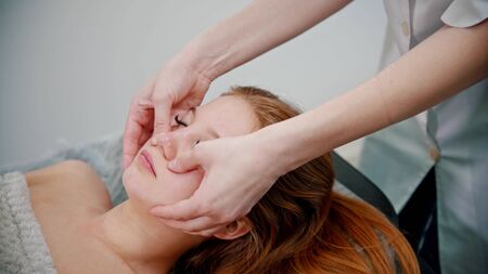 Massage - omassage therapist massaging the face of a red-haired woman with her hands