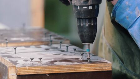 Concrete workshop - a man with a screwdriver screwing the bolts into a wooden surface - indoor