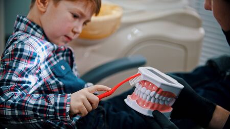 A little boy in the dentistry - brushing teeth of the plastic model of human jaws