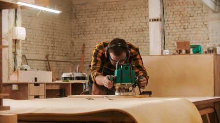 Carpentry industry - worker in protective glasses and headphones grinding a wooden item in the workshopの写真素材