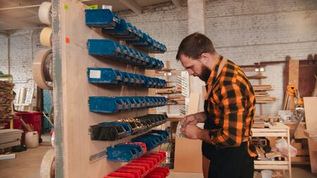 Carpentry workshop - bearded man worker choosing screws from the standの写真素材