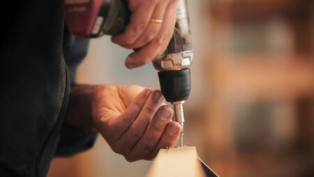 Carpentry - worker drills a screw into the wooden plankの写真素材