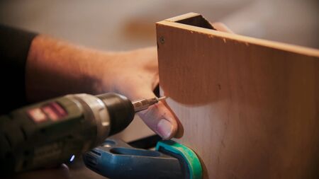 Carpentry - worker drills holes into the piece of plywood. Mid shot