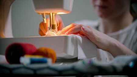 Young woman designer sewing a reusable mask using a sewing machine. Mid shot