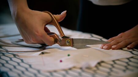 Young woman seamstress cutting white cloth with big scissorsの写真素材
