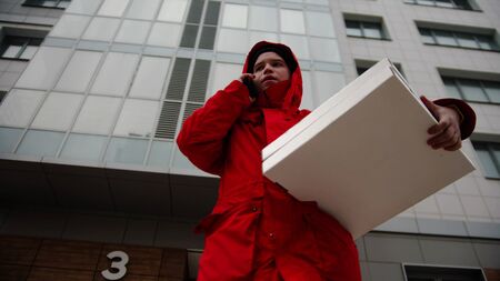 A man courier delivering pizza - holding two boxes and talking on the phone