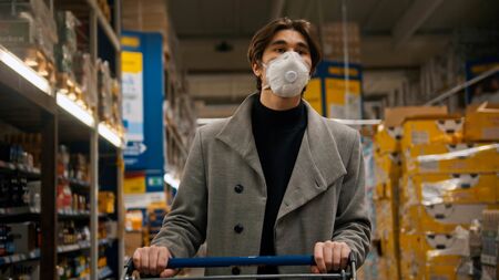 Young man in protective mask and grey coat pushing the pushcartの写真素材