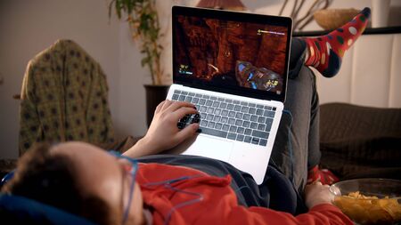 Young man lying on the bed playing shooter video game on the laptop