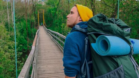 Young man traveler in yellow hat with a big backpack walking on the bridgeの写真素材