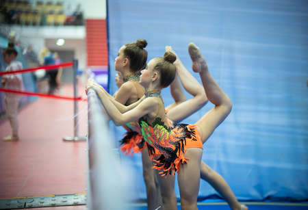 12-03-2020 KAZAN, RUSSIA: teen girls in bright orange costumes training near the bar before the gymnastic tournamentのeditorial素材