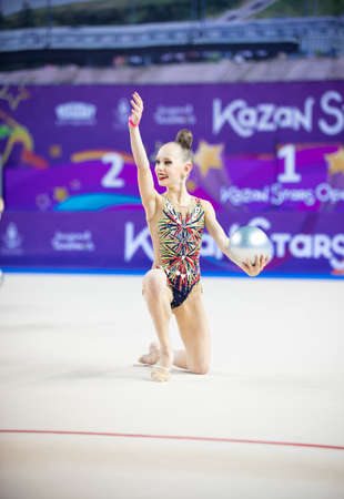12-03-2020 KAZAN, RUSSIA: slim teen girl in bright colorful swim costume performing with silver ball on the gymnastic tournamentのeditorial素材