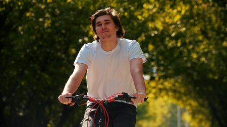 Young smiling happy man in white shirt riding a bikeの写真素材