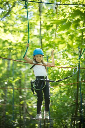 Rope adventure in the forest - a little girl standing on the bridge with full insurance and having...