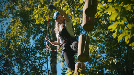 Woman crossing a construction of the rope and stumps - an entertainment attraction in the green...