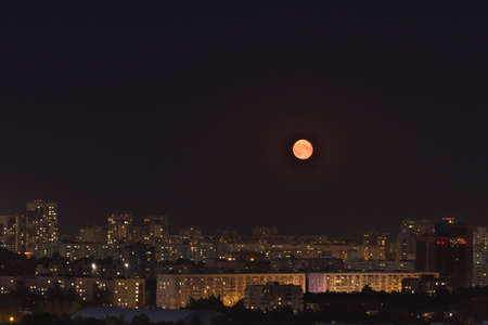 Bright yellow moon in dark almost black sky above the city