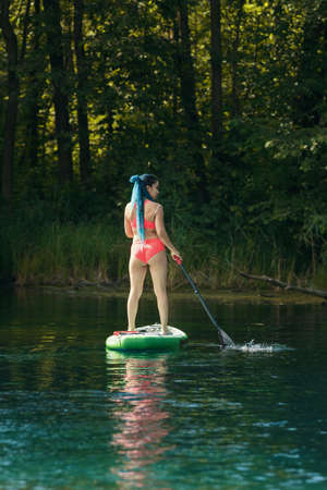 Woman with blue braids standing on an inflatable boat on river and holding a paddle